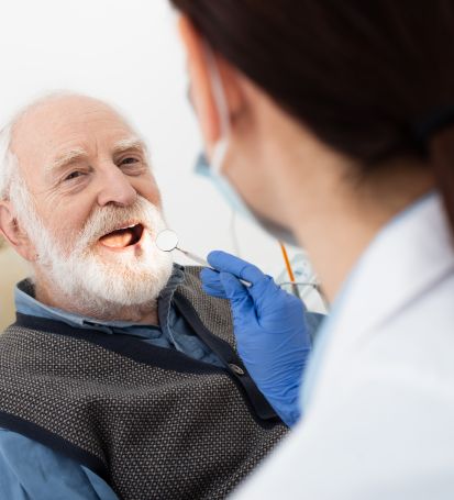 Older man in dentist’s chair receiving treatment covered by private dental insurance