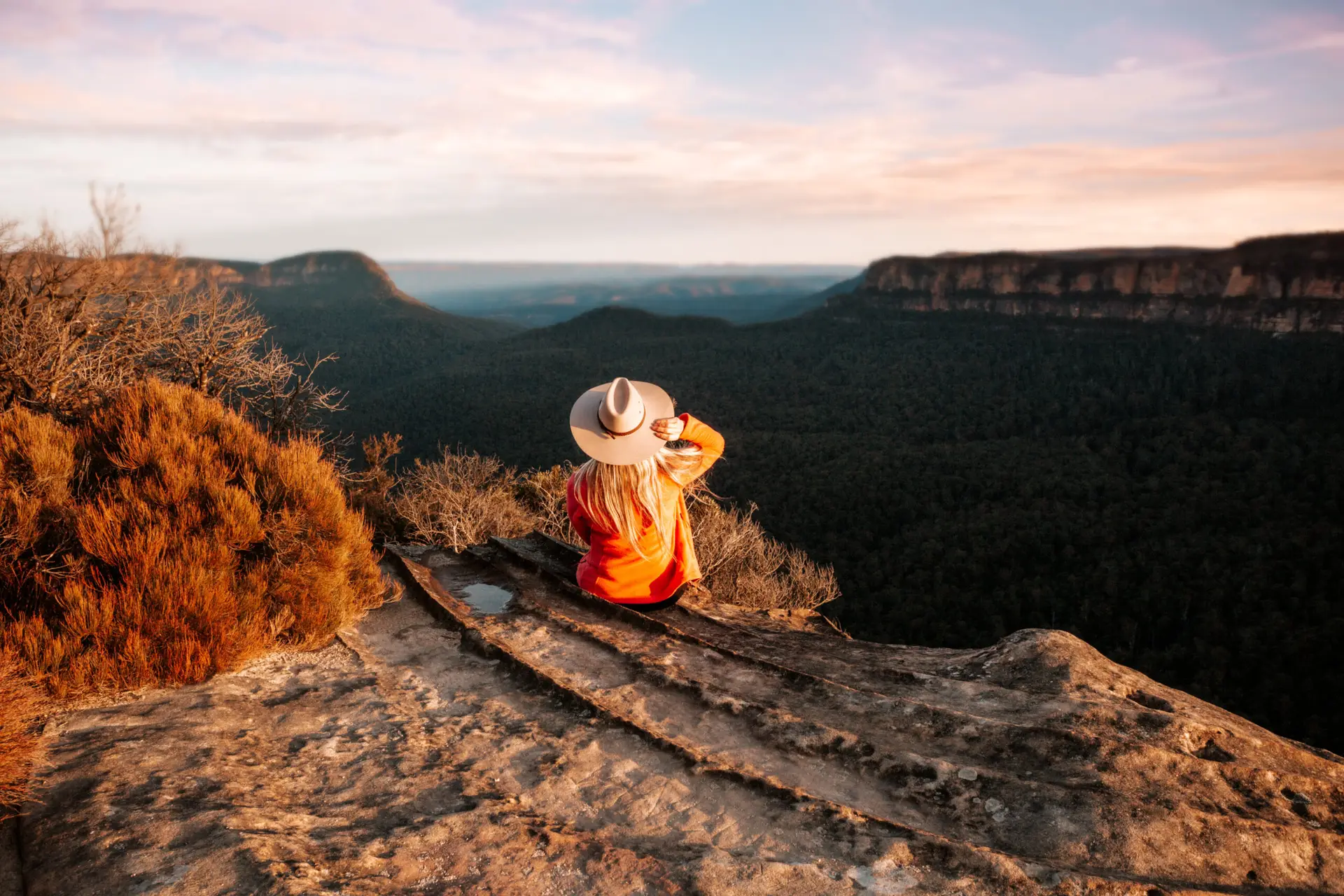 Woman sits on the edge of a cliff and looks out over the mountains in a late afternoon